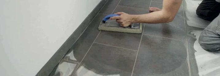 Person verfugt Fliesen mit einem Fugschwamm.